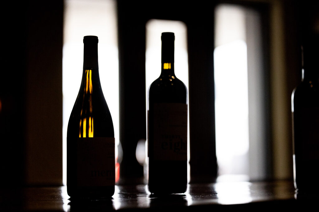 Wine bottles backlit by windows within darkly lit room Wine bottles backlit by windows within darkly lit room